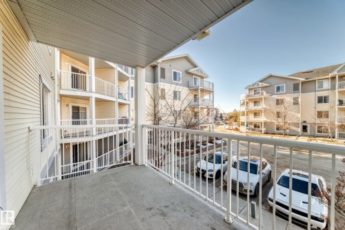 The property features a private balcony with a white railing, offering views of similar residential buildings and a parking area - 208 2204 44 Ave, Edmonton, AB - Outdoor With Balcony With Exterior