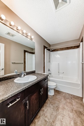 Bathroom featuring a dark wood vanity with a light-colored countertop, a white sink, and a large mirror with vanity lighting - 208 2204 44 Ave, Edmonton, AB - Indoor Photo Showing Bathroom