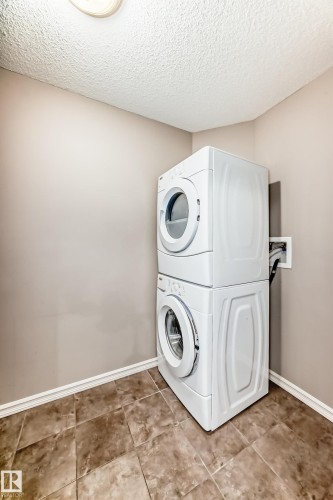 The property includes a laundry area featuring a white stacked washer and dryer unit, set on durable tile flooring - 208 2204 44 Ave, Edmonton, AB - Indoor Photo Showing Laundry Room