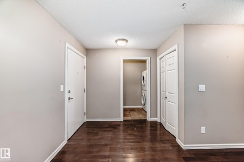 Entryway featuring rich hardwood flooring, light neutral-toned walls, and a convenient laundry area with a stacked washer and dryer - 208 2204 44 Ave, Edmonton, AB - Indoor Photo Showing Other Room