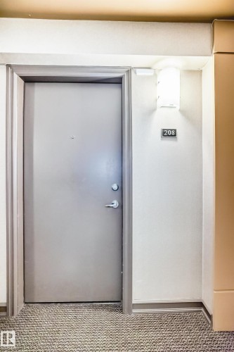 Entry door with a modern handle and deadbolt, situated in a carpeted hallway with a wall sconce - 208 2204 44 Ave, Edmonton, AB - Indoor Photo Showing Other Room