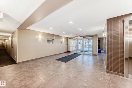 The building entrance features glass doors, tiled flooring, and a long hallway with wall-mounted lighting fixtures - 208 2204 44 Ave, Edmonton, AB - Indoor Photo Showing Other Room