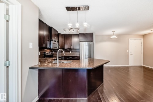 The property features a kitchen with dark cabinetry, granite countertops, and stainless steel appliances, including a microwave and refrigerator - 208 2204 44 Ave, Edmonton, AB - Indoor Photo Showing Kitchen With Double Sink