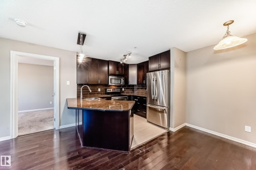 The kitchen features dark wood cabinetry, stainless steel appliances, and a granite-topped island with an undermount sink - 208 2204 44 Ave, Edmonton, AB - Indoor Photo Showing Kitchen