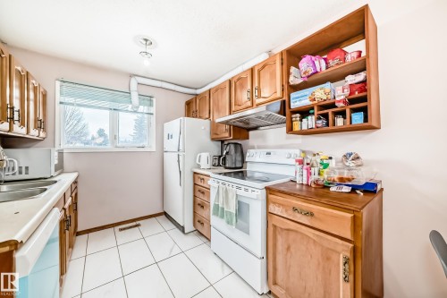 The kitchen features wood cabinetry, a white refrigerator, a white electric range, and white tiled flooring - 11393 22 Avenue, Edmonton, AB - Indoor Photo Showing Kitchen