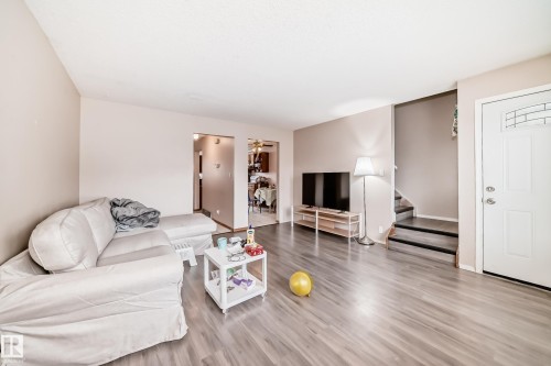 Living area featuring light-toned flooring, neutral wall paint, and a white front entry door with a decorative window pane - 11393 22 Avenue, Edmonton, AB - Indoor Photo Showing Living Room