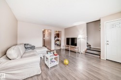 Living area featuring light-toned flooring, neutral wall paint, and a white front entry door with a decorative window pane - 