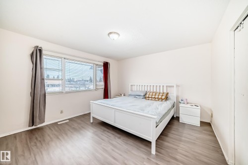 This room features light-toned walls, wood-look flooring, and a large window with horizontal blinds and curtains - 11393 22 Avenue, Edmonton, AB - Indoor Photo Showing Bedroom