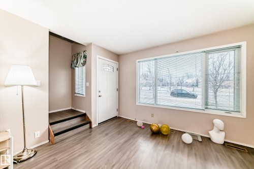 The property features durable flooring, a large window providing natural light, and a white entry door with decorative glass inserts - 11393 22 Avenue, Edmonton, AB - Indoor Photo Showing Other Room