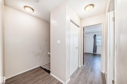Hallway featuring light-toned walls, overhead lighting, and wood-look flooring - 