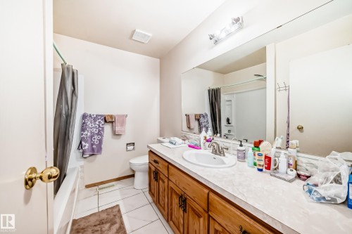 Bathroom featuring a vanity with a white countertop and wood cabinetry, a large wall-mounted mirror, and a toilet - 11393 22 Avenue, Edmonton, AB - Indoor Photo Showing Bathroom