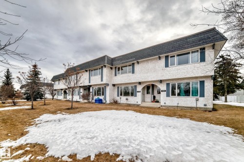 The property features a multi-unit structure with a dark roof and white exterior, accented by blue window shutters - 11393 22 Avenue, Edmonton, AB - Outdoor