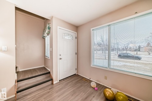 The property features a main entrance with a white door, a large window with blinds, and light-toned flooring - 11393 22 Avenue, Edmonton, AB - Indoor Photo Showing Other Room