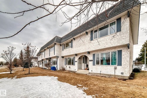 The property features a stucco exterior, dark shingled roof, and blue window shutters - 11393 22 Avenue, Edmonton, AB - Outdoor