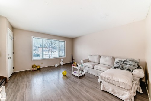 This room features durable plank flooring, light-colored walls, and a large window providing ample natural light - 11393 22 Avenue, Edmonton, AB - Indoor Photo Showing Living Room