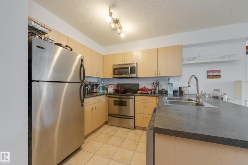The kitchen features stainless steel appliances, light-toned cabinetry, and dark countertops - 1007 10180 104 Street, Edmonton, AB - Indoor Photo Showing Kitchen With Double Sink