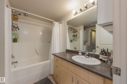 The bathroom features a white vanity with a rectangular sink and chrome faucet, a white bathtub with a shower and curtain, and a wall-mounted mirror with overhead lighting - 