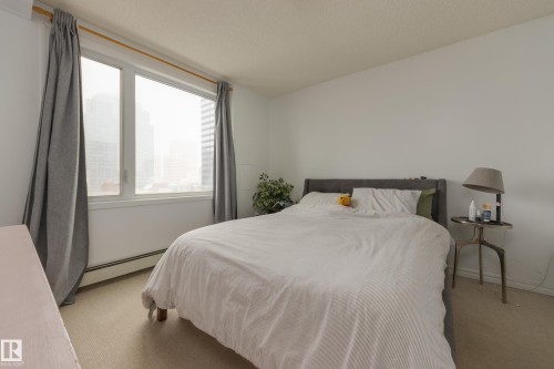 This room features a large window with white trim, light-colored walls, and neutral carpet flooring - 1007 10180 104 Street, Edmonton, AB - Indoor Photo Showing Bedroom