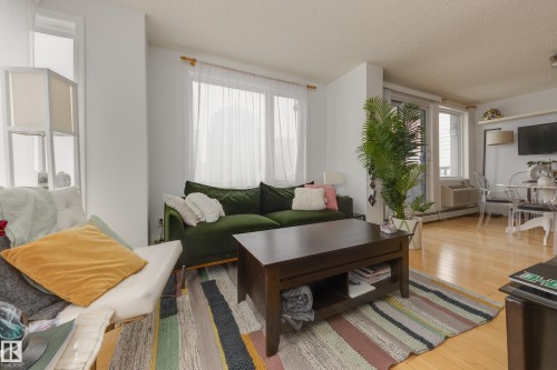 Living area featuring light wood flooring, large windows with white sheer curtains, and a glass sliding door providing natural light - 1007 10180 104 Street, Edmonton, AB - Indoor