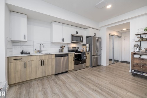 The kitchen features a stainless steel refrigerator, microwave, and range - 101 860 Secord Blvd, Edmonton, AB - Indoor Photo Showing Kitchen With Stainless Steel Kitchen