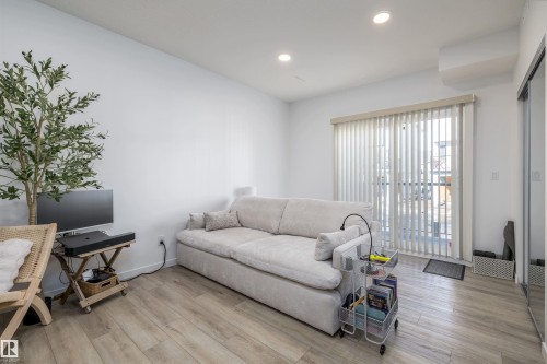 This living area features light-toned flooring, recessed ceiling lights, and a sliding glass door with vertical blinds - 101 860 Secord Blvd, Edmonton, AB - Indoor