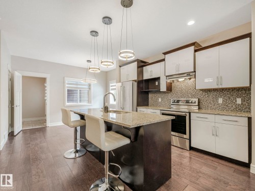 The property features a kitchen with an island, pendant lighting, stainless steel appliances, a tile backsplash, and light-colored cabinetry - 2 10319 120 Street, Edmonton, AB - Indoor Photo Showing Kitchen With Upgraded Kitchen