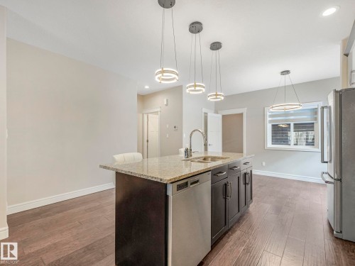Kitchen featuring an island with a granite countertop, a stainless steel sink, and a built-in dishwasher - 2 10319 120 Street, Edmonton, AB - Indoor Photo Showing Kitchen With Double Sink With Upgraded Kitchen