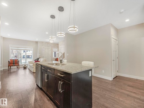 The kitchen features a dark wood island with a granite countertop, a stainless steel sink with a gooseneck faucet, and three modern pendant lights - 2 10319 120 Street, Edmonton, AB - Indoor Photo Showing Kitchen With Double Sink