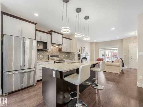 The kitchen features stainless steel appliances, upper and lower cabinetry, and a central island with a granite countertop and integrated sink - 2 10319 120 Street, Edmonton, AB - Indoor Photo Showing Kitchen With Upgraded Kitchen