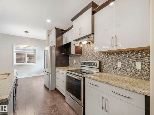 The kitchen features bright white cabinetry with granite countertops, stainless steel appliances, and a mosaic tile backsplash - 2 10319 120 Street, Edmonton, AB - Indoor Photo Showing Kitchen With Upgraded Kitchen