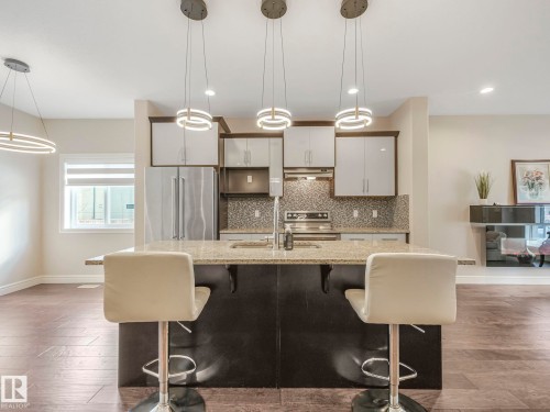 Open concept kitchen featuring an island with a light-colored countertop, stainless steel appliances, and ceiling-mounted light fixtures - 2 10319 120 Street, Edmonton, AB - Indoor Photo Showing Kitchen With Upgraded Kitchen