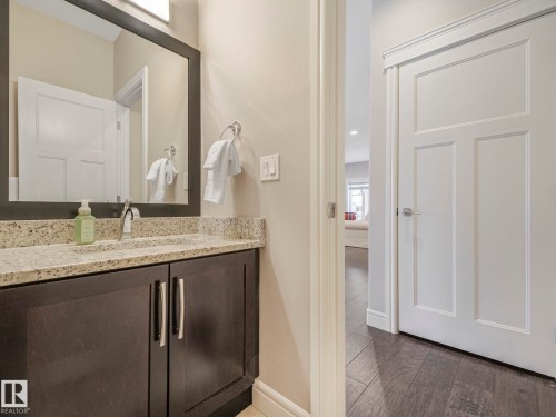 Bathroom vanity with a granite countertop, a dark wood cabinet, and a large framed mirror - 2 10319 120 Street, Edmonton, AB - Indoor Photo Showing Bathroom