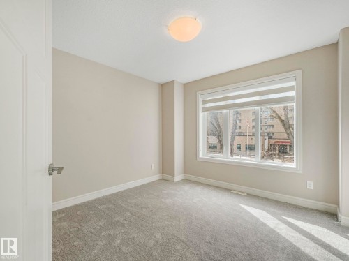 This room features neutral-toned walls, grey carpet, and a window with blinds - 2 10319 120 Street, Edmonton, AB - Indoor Photo Showing Other Room