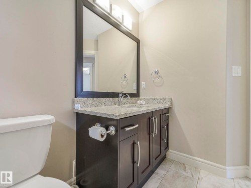 Bathroom featuring a dark wood vanity with a light granite countertop, a rectangular mirror with overhead lighting, and tiled flooring - 2 10319 120 Street, Edmonton, AB - Indoor Photo Showing Bathroom