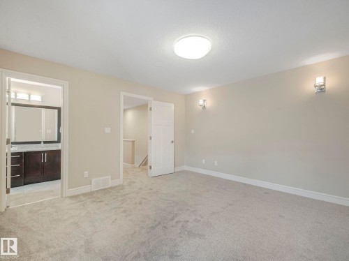 Spacious room featuring light-colored carpet, neutral wall paint, and wall sconces, with a bathroom visible through an open doorway - 2 10319 120 Street, Edmonton, AB - Indoor Photo Showing Other Room