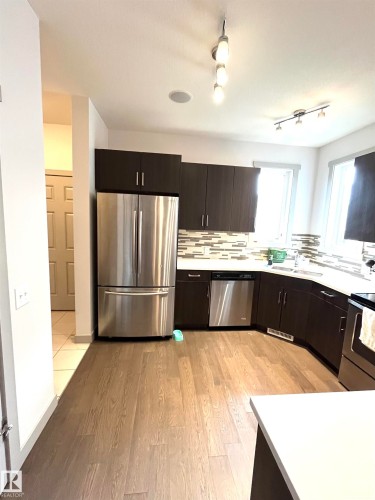 Well-appointed kitchen featuring stainless steel appliances, dark cabinetry, and light wood flooring - 16464 15 Avenue, Edmonton, AB - Indoor Photo Showing Kitchen With Stainless Steel Kitchen With Upgraded Kitchen