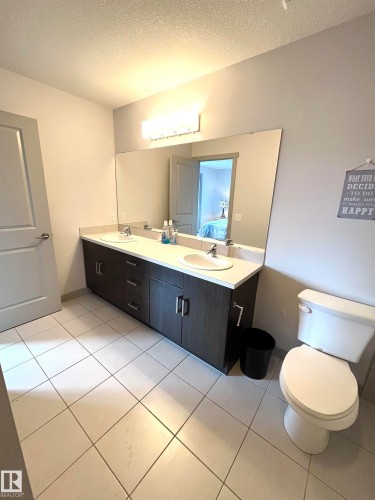 The bathroom features a double vanity with two sinks and a spacious mirror, complemented by a white toilet - 16464 15 Avenue, Edmonton, AB - Indoor Photo Showing Bathroom