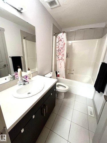 Bathroom featuring a vanity with a white countertop and dark cabinetry, a built-in bathtub with shower, and tiled flooring - 16464 15 Avenue, Edmonton, AB - Indoor Photo Showing Bathroom