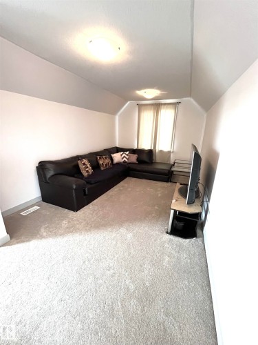 This inviting space features light-colored carpeting, sloped ceilings, and a window with light-colored curtains - 16464 15 Avenue, Edmonton, AB - Indoor Photo Showing Other Room