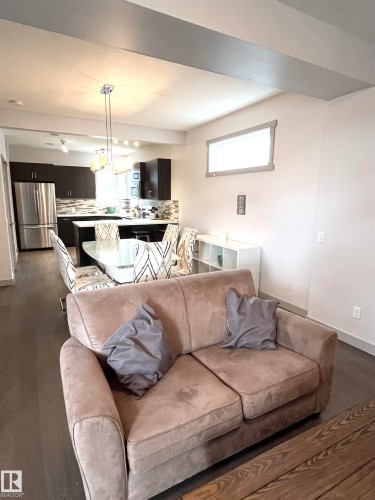 The open concept living area features hardwood floors and a view of the kitchen with dark cabinetry and stainless steel appliances - 16464 15 Avenue, Edmonton, AB - Indoor Photo Showing Living Room