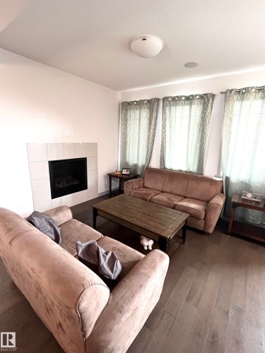 Living area featuring a fireplace with white tile surround, dark wood-style flooring, and recessed ceiling speakers - 16464 15 Avenue, Edmonton, AB - Indoor Photo Showing Living Room With Fireplace