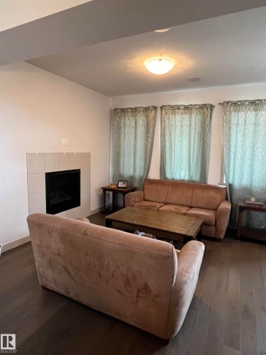 The property features a living area with dark hardwood floors, a tiled fireplace, and a ceiling light fixture - 16464 15 Avenue, Edmonton, AB - Indoor Photo Showing Living Room With Fireplace