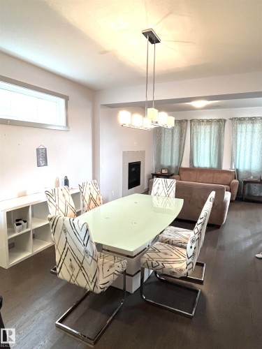 Dining area featuring dark wood flooring, a linear chandelier, and a white modern fireplace - 16464 15 Avenue, Edmonton, AB - Indoor