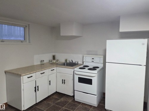 Kitchen featuring white appliances, white cabinets, light countertops, and dark tile patterned floors - 13023 Sherbrooke Avenue, Edmonton, AB - Indoor Photo Showing Kitchen