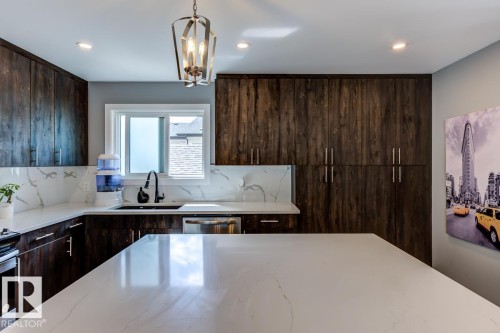 This kitchen features an expansive island with a white countertop, dark wood cabinetry, a white countertop and backsplash, and a modern light fixture - 9526 109A Avenue, Edmonton, AB - Indoor Photo Showing Kitchen With Upgraded Kitchen