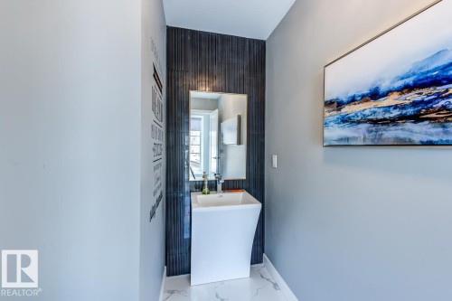 This powder room features a contemporary pedestal sink, a wall-mounted mirror, and dark textured wall tiles - 9526 109A Avenue, Edmonton, AB - Indoor