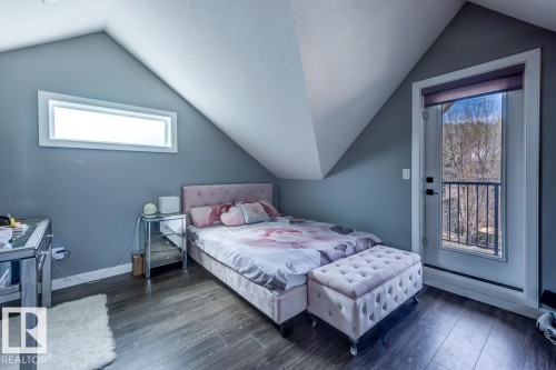 This room features wood flooring, a window offering natural light, and a door that opens to a balcony with a black metal railing - 9526 109A Avenue, Edmonton, AB - Indoor Photo Showing Bedroom