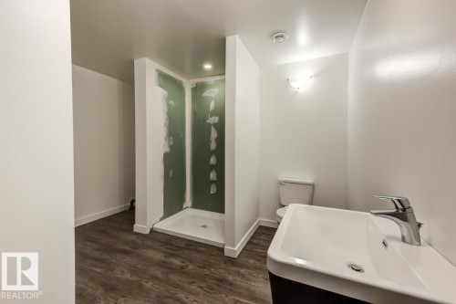 This bathroom features wood-look flooring, a white toilet, a modern sink with a chrome faucet, and a shower area with a white base - 9526 109A Avenue, Edmonton, AB - Indoor Photo Showing Bathroom