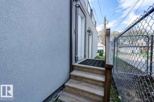 Exterior view featuring a light-colored stucco wall, wooden stairs with a handrail, and an outdoor light fixture beside an entrance - 9526 109A Avenue, Edmonton, AB - Outdoor