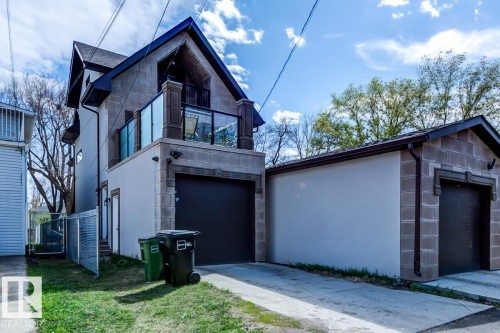 Exterior view of the property featuring a garage with a dark door, a second-story balcony with glass railings, and an additional detached garage structure - 9526 109A Avenue, Edmonton, AB - Outdoor
